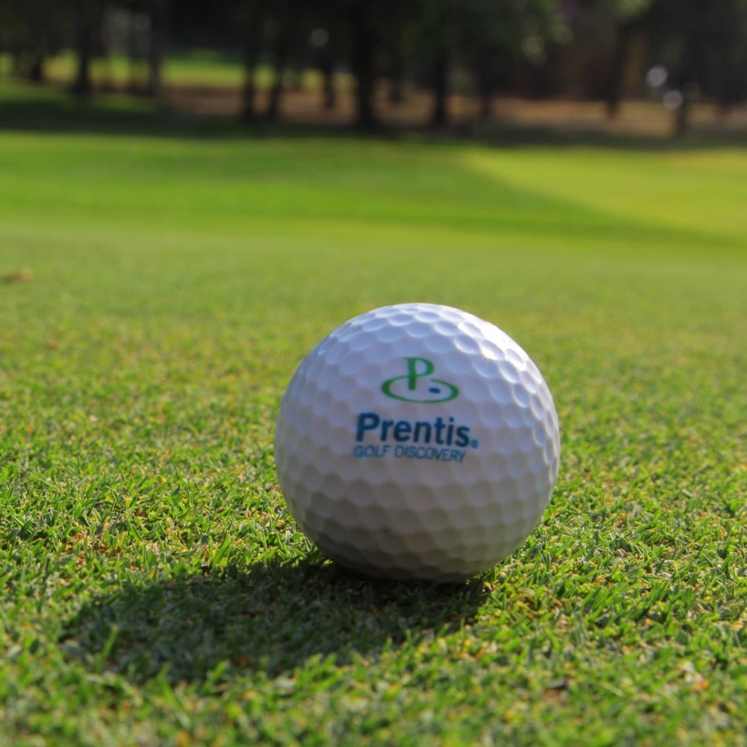 A Prentis Golf ball on a sunny fairway with trees behind