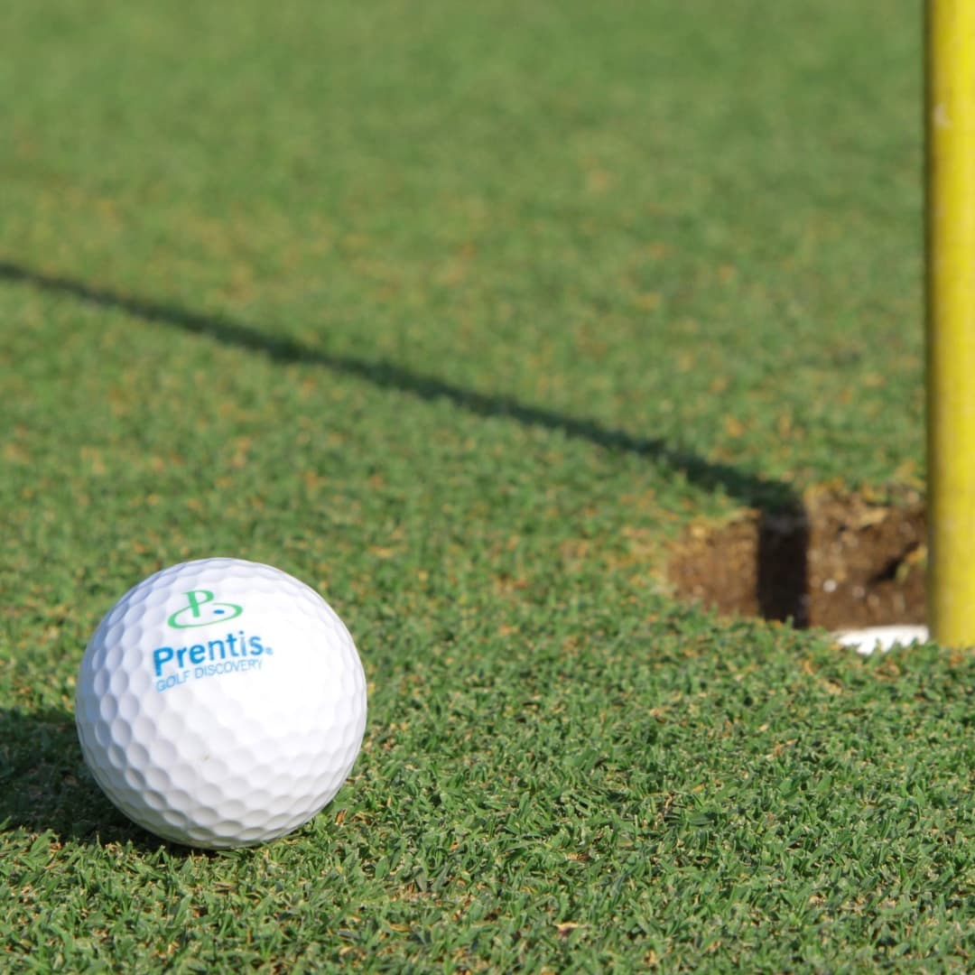 A Prentis Golf branded ball resting on the green a few inches from the hole