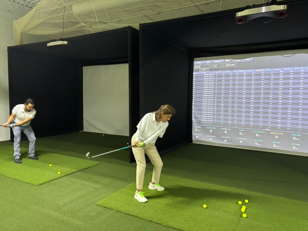 Dos alumnos de Prentis Golf haciendo swing en tapetes bajo techo frente a una pantalla con los datos de sus golpes