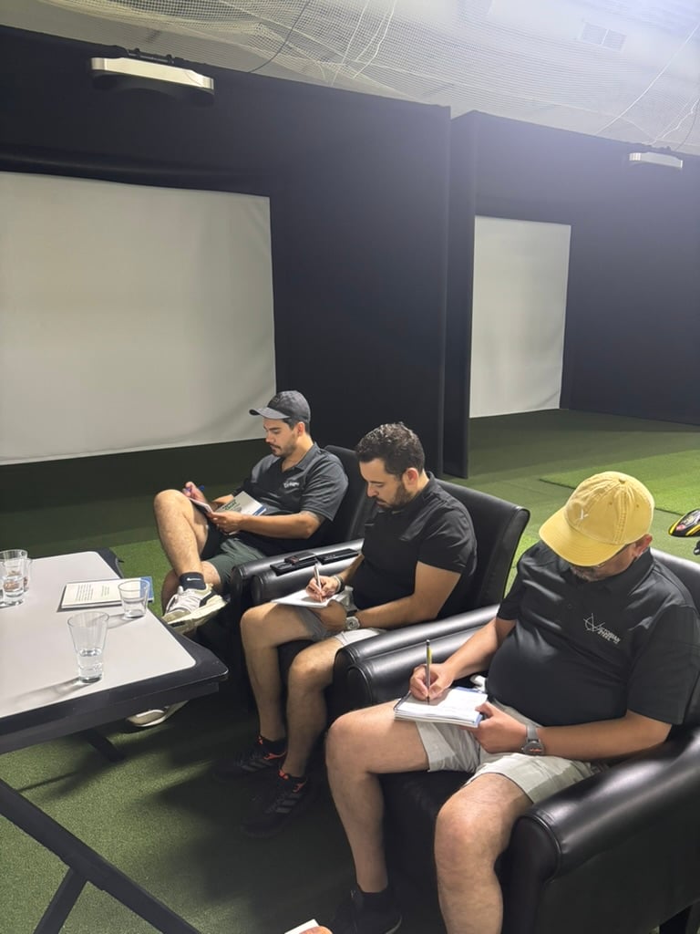 Tres alumnos de Prentis Golf con polos negros tomando notas en sillones de piel frente a las pantallas del simulador