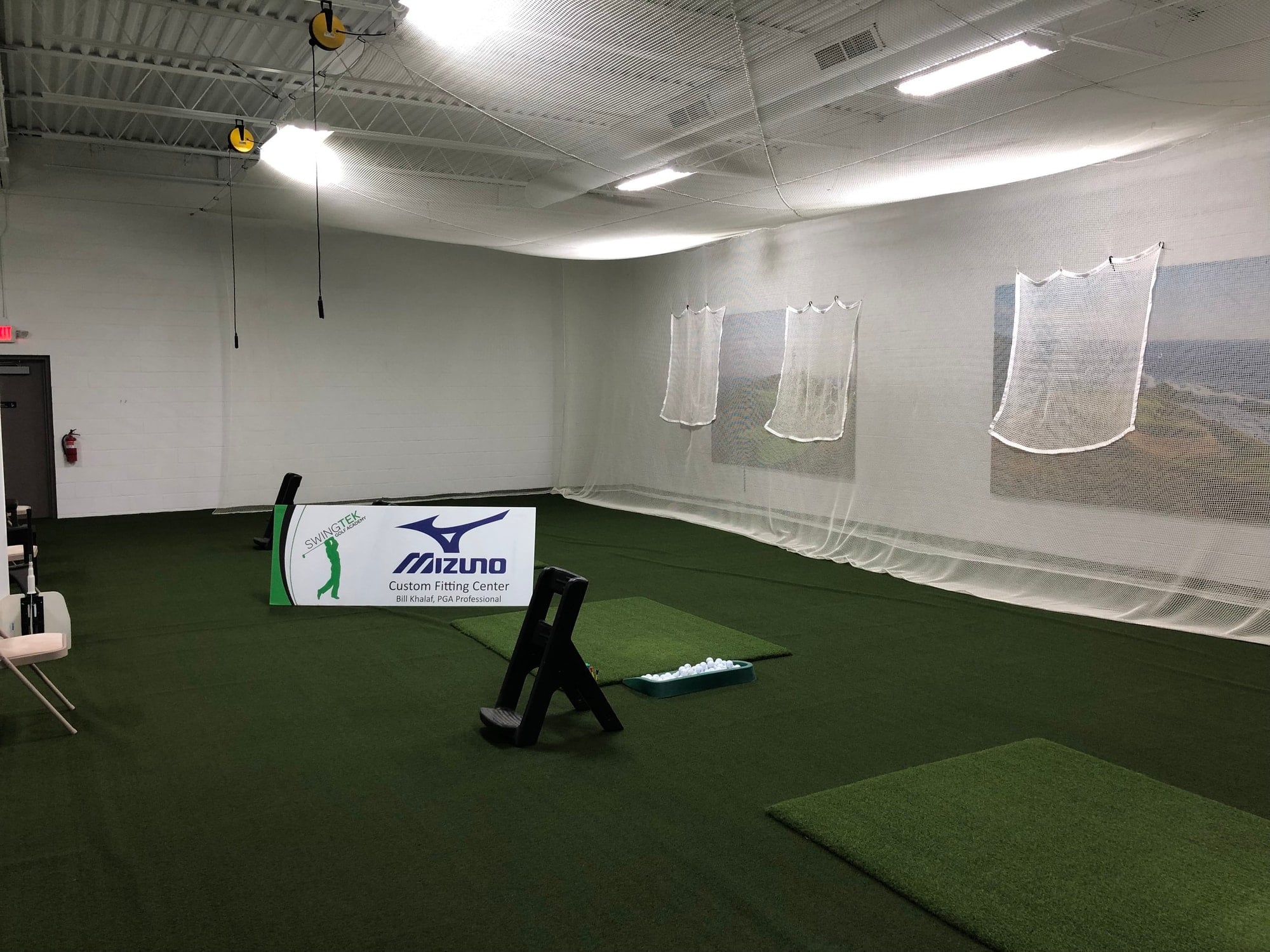 Indoor hitting bays with practice mats, a tray of balls and catch nets along the wall